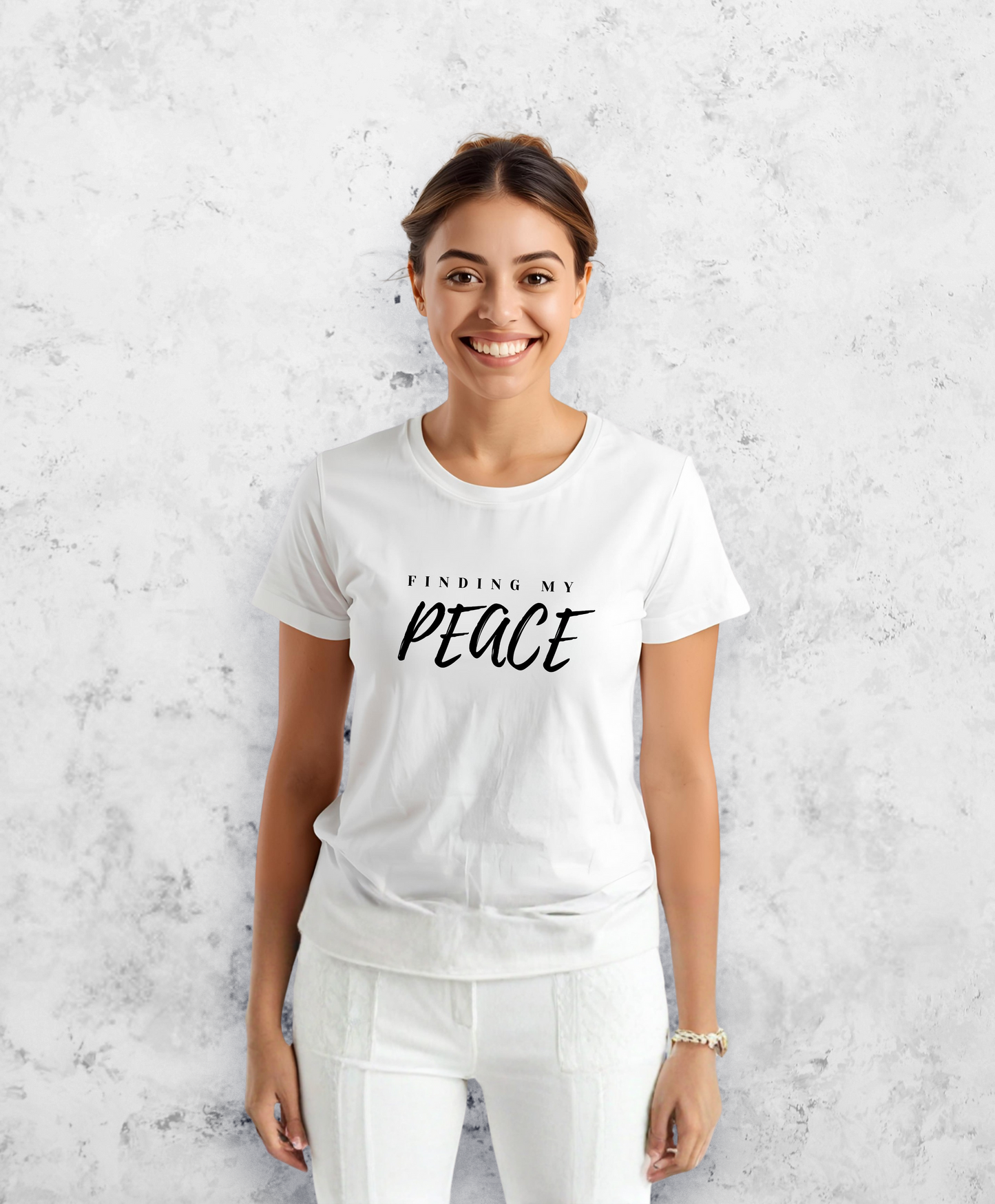 Uśmiechnięta kobieta, stojąca przodem do kamery, ubrana w biały t-shirt, koszulkę, z czarnym napisem "Finding my peace"