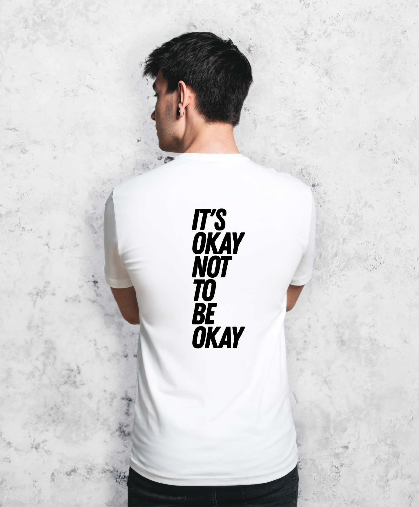 Zdjęcie przedstawia mężczyznę stojącego tyłem do kamery. Ma na sobie białą koszulkę z czarnym napisem "It's ok not to be ok".