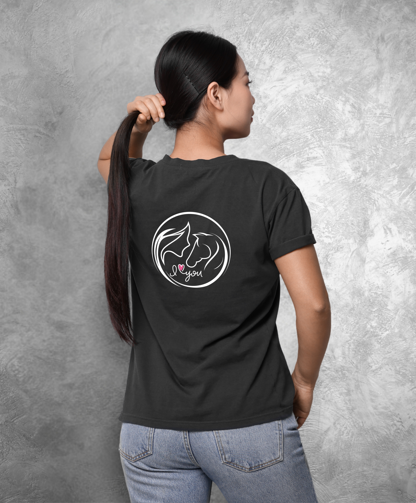 Zdjęcie przedstawia kobietę stojącą tyłem do kamery. Ubrana jest w czarny t-shirt z nadrukiem na plecach. Nadruk przedstawia koło z graficznie pokazaną głową kobiety i konia z profilu oraz napis I love you, gdzie słowo "love" przedstawione jest jako różowe serce. Reszta nadruku jest w kolorze białym.