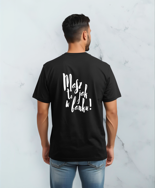 Mężczyzna stojący tyłem do kamery. Ubrany w czarną koszulkę z białym napisem "Masz to jak w banku" na plecach