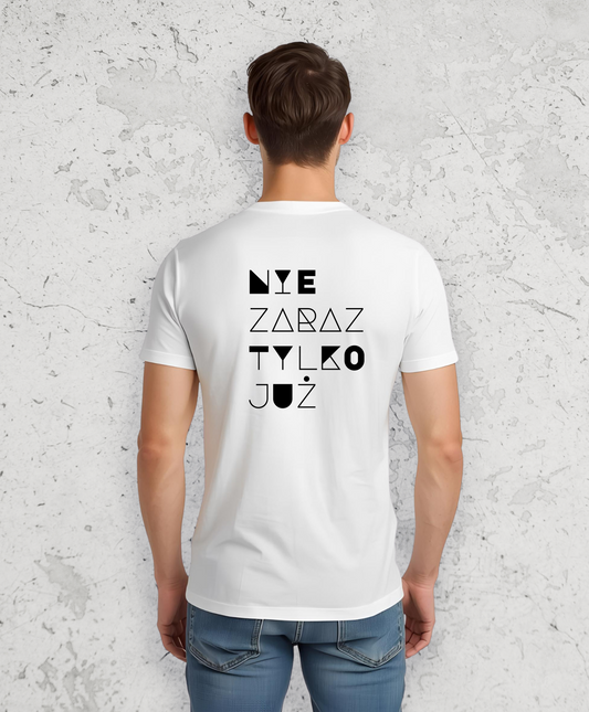 Mężczyzna stojący tyłem do kamery. Ubrany w biały t-shirt z czarnym napisem na plecach "Nie zaraz, tylko już"
