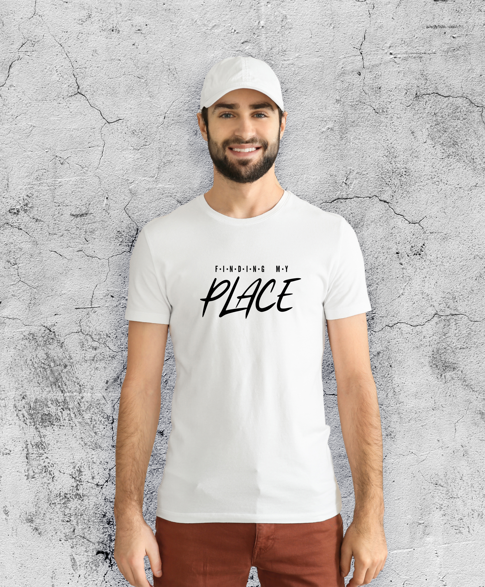 Uśmiechnięty mężczyzna stojący przodem do kamery, ubrany w białą koszulkę z czarnym napisem "Finding my place".