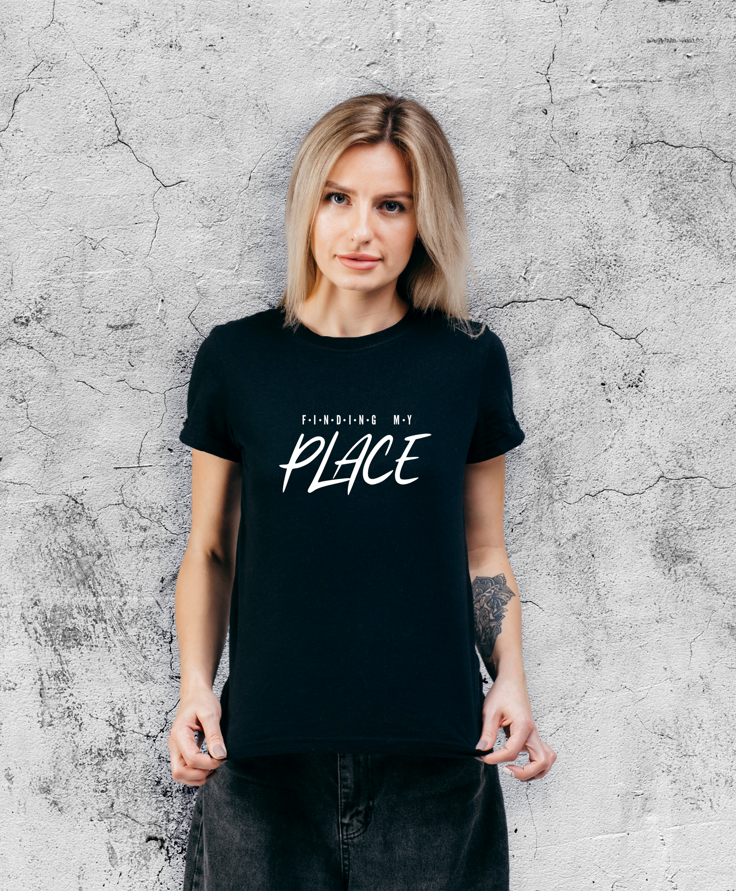 Uśmiechnięta kobieta stojąca przodem do kamery, ubrana w czarną koszulki z białym napisem "Finding my place".
