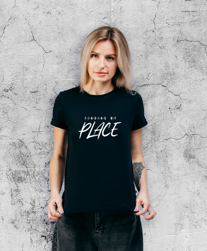 Uśmiechnięta kobieta stojąca przodem do kamery, ubrana w czarną koszulki z białym napisem "Finding my place".