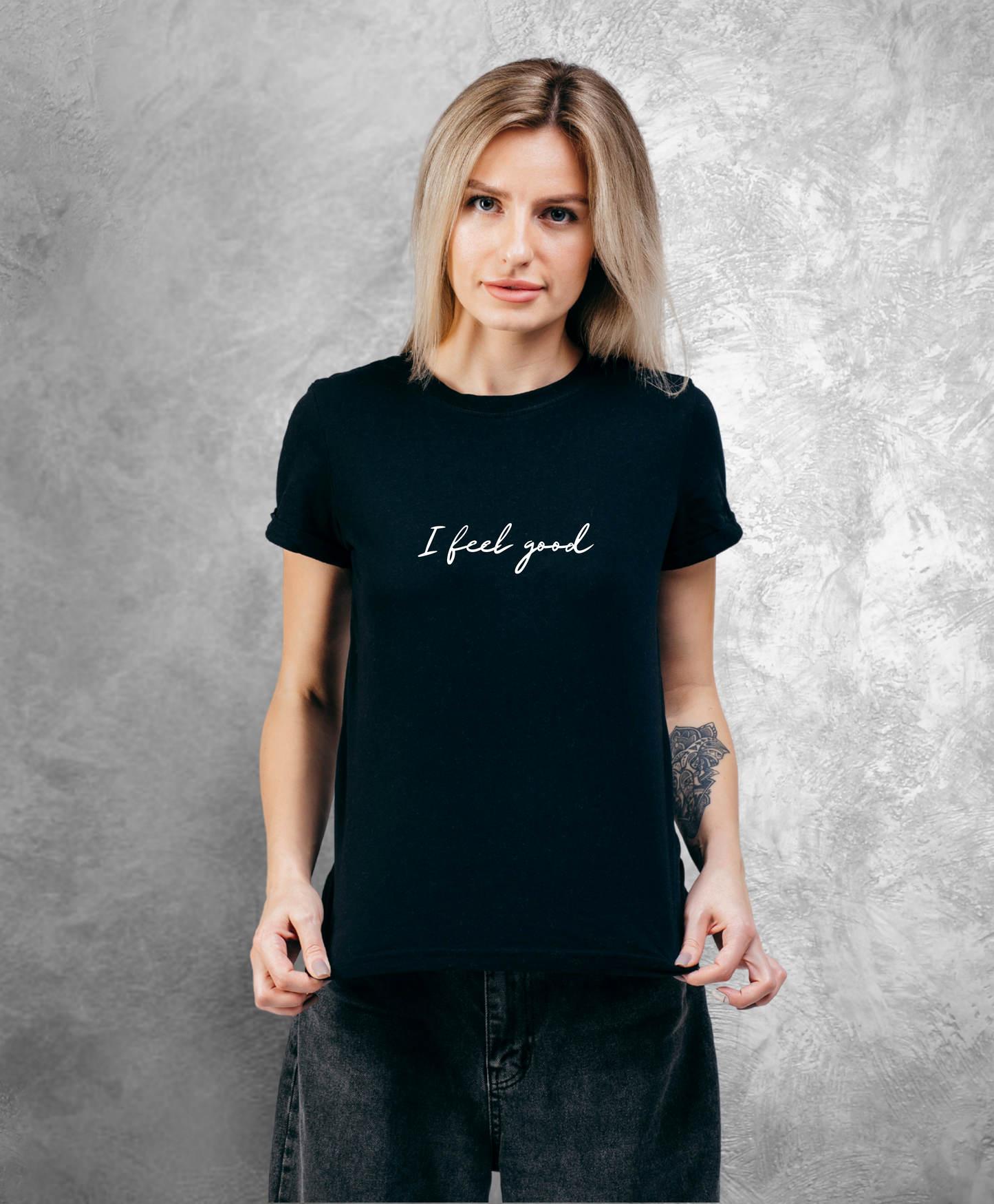 Pozująca do kamery kobieta stojąca przodem do kamery ubrana w czarny t-shirt z białym napisem "I feel good"