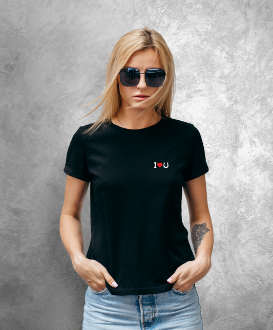 Kobieta stojąca przodem do kamery. Ma na sobie czarną koszulkę z białym napisem "I love horses" gdzie słowo "love" przedstawione jest jako czerwone serce, a słowo "horses" jako czarna podkowa.  