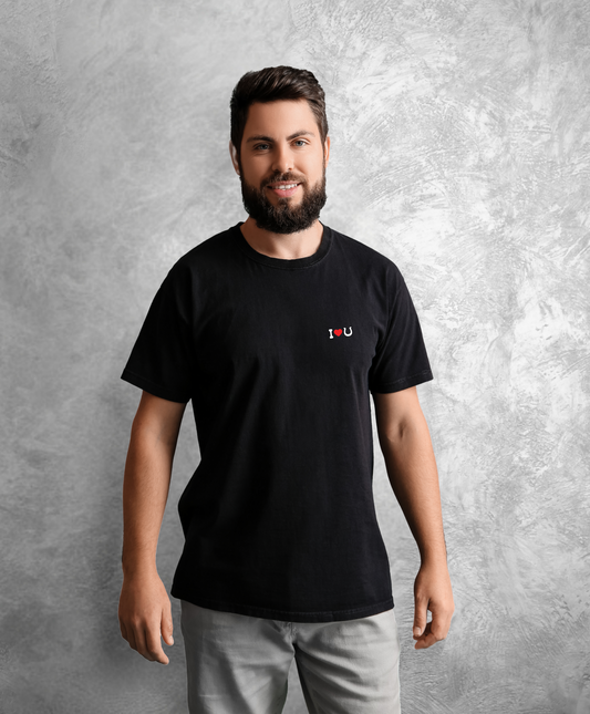 Mężczyzna stojący przodem do kamery. Ma na sobie czarną koszulkę z białym napisem "I love horses" gdzie słowo "love" przedstawione jest jako czerwone serce, a słowo "horses" jako czarna podkowa.  