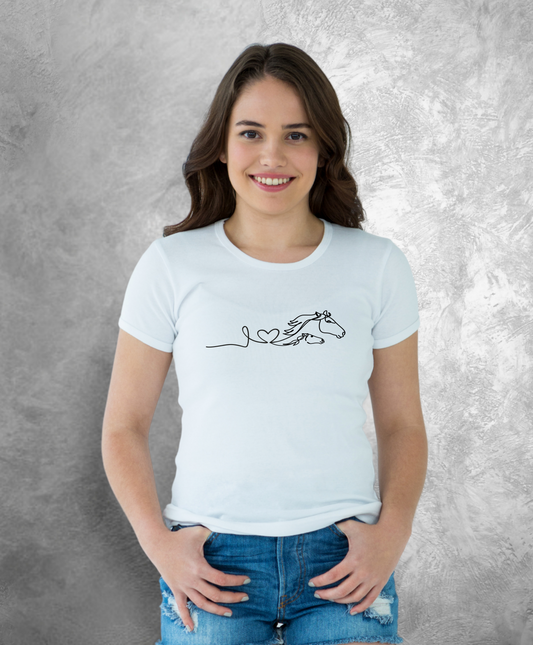 Uśmiechnięta kobieta stojąca przodem do kamery, ubrana w białą koszulkę z czarnym nadrukiem przedstawiającym dwa konie i napis układający się w napis " love horses"