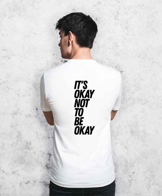 Zdjęcie przedstawia mężczyznę stojącego tyłem do kamery. Ma na sobie białą koszulkę z czarnym napisem "It's ok not to be ok". 