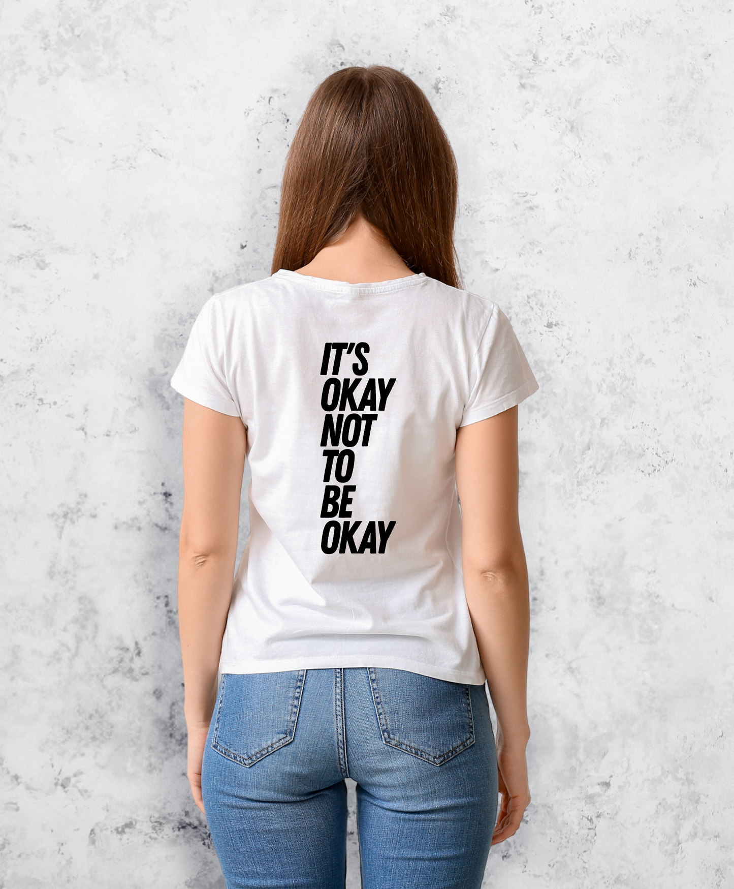 Zdjęcie przedstawia kobietę stojącą tyłem do kamery. Ma na sobie białą koszulkę z czarnym napisem "It's ok not to be ok". 