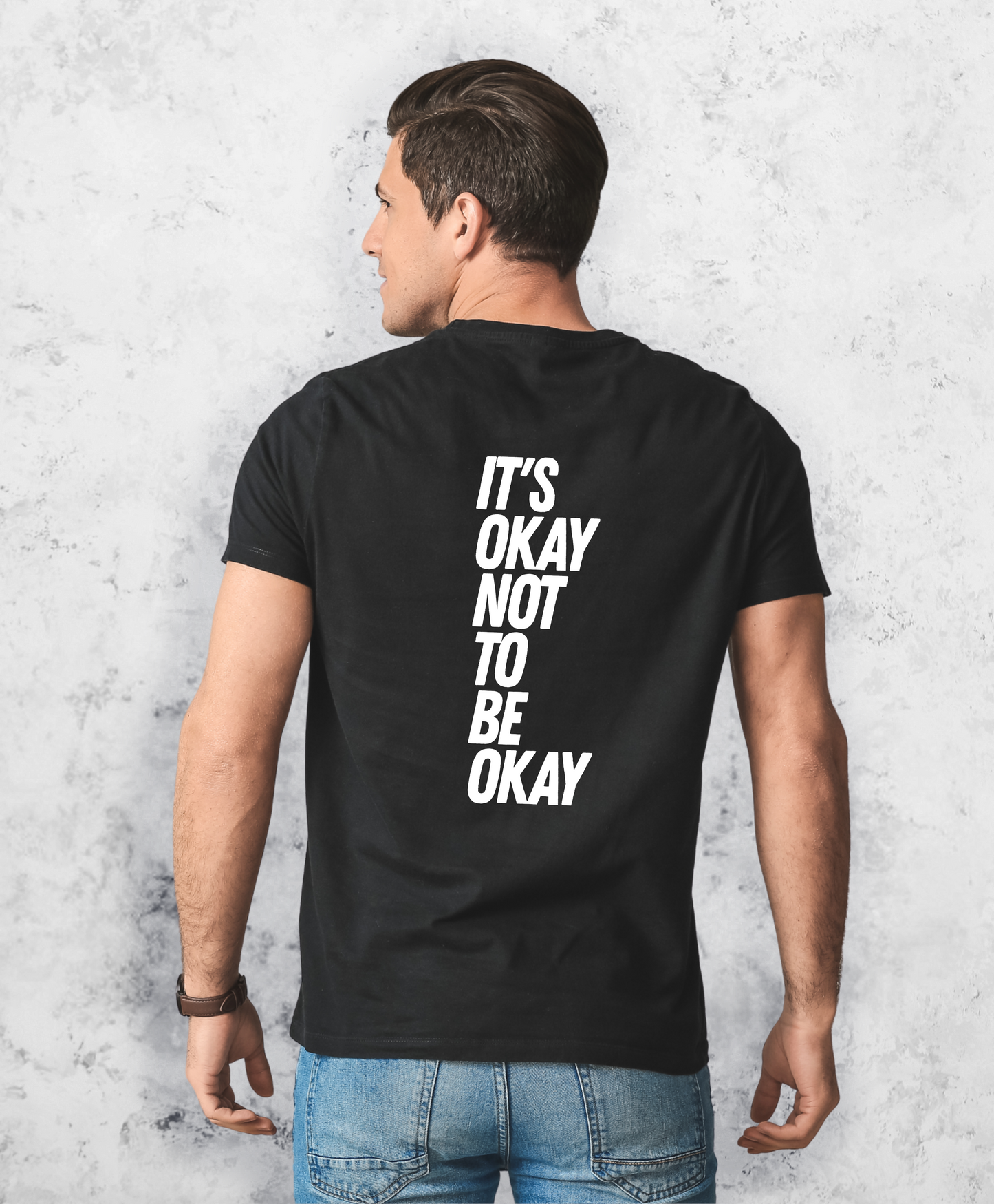 Zdjęcie przedstawia mężczyznę stojącego tyłem do kamery. Ma na sobie czarną koszulkę z białym napisem "It's ok not to be ok". 