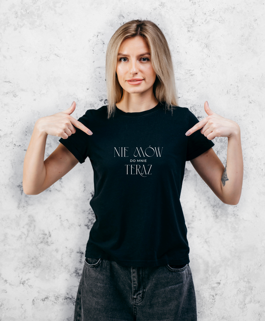 Zdjęcie przedstawia uśmiechniętą kobietę w czarnej koszulce z białym napisem "Nie mów do mnie teraz". 