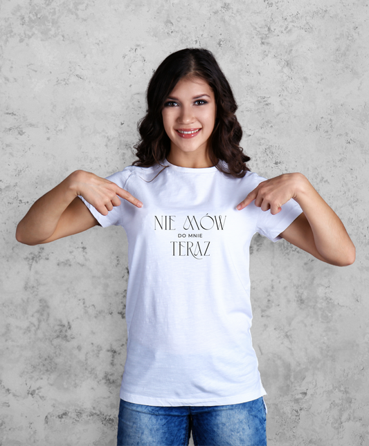 Zdjęcie przedstawia uśmiechniętą kobietę w białej koszulce z czarnym napisem "Nie mów do mnie teraz". 