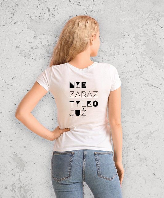 Kobieta stojąca tyłem do kamery. Ubrana w biały t-shirt z czarnym napisem na plecach "Nie zaraz, tylko juz"