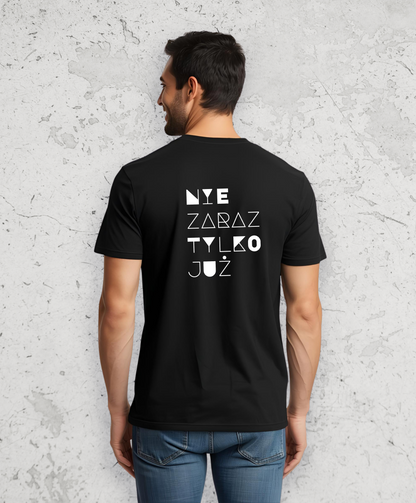 Mężczyzna stojący tyłem do kamery. Ubrany w czarny t-shirt z białym napisem na plecach "Nie zaraz, tylko już"