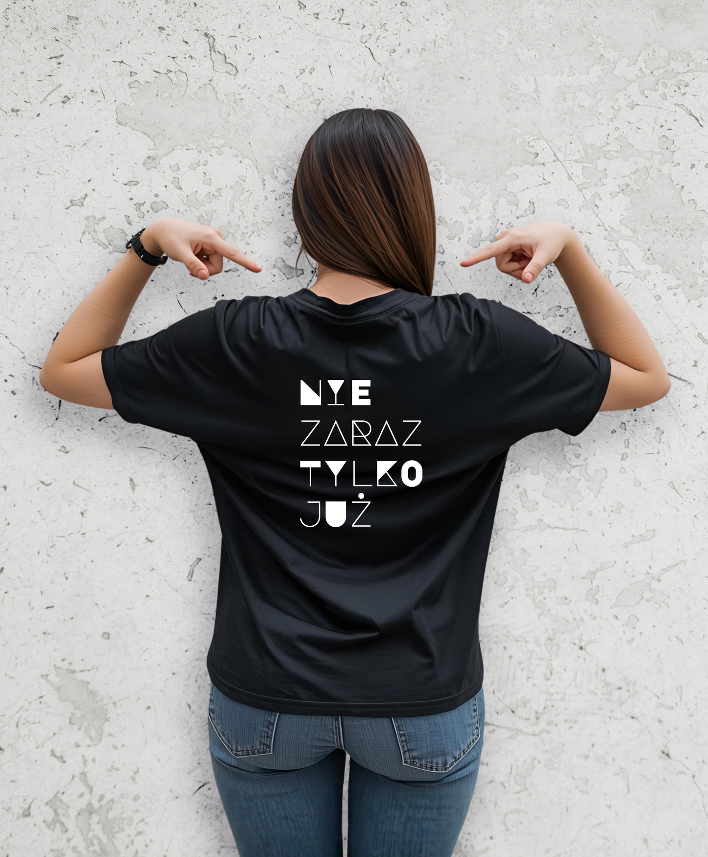 Kobieta stojąca tyłem do kamery. Ubrana w czarny t-shirt z białym napisem na plecach "Nie zaraz, tylko juz"
