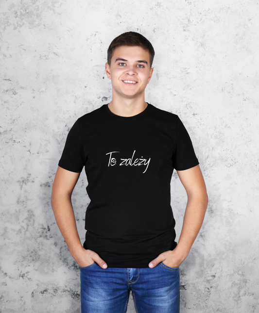 Zdjęcie przedstawia uśmiechniętego mężczyznę, stojącego przodem do kamery, ubranego w czarną koszulkę z białym napisem na przodzie "To zależy"