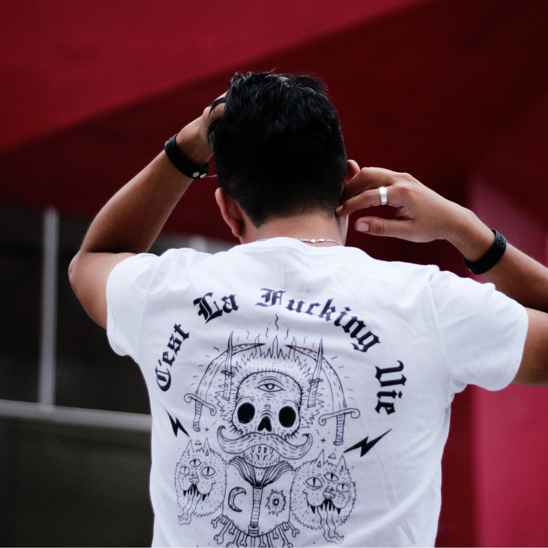 zdjęcie przedstawia odwróconego plecami mężczyznę z białej koszulce z czarną, rysunkową grafiką przedstawiającą miecze i czaszki