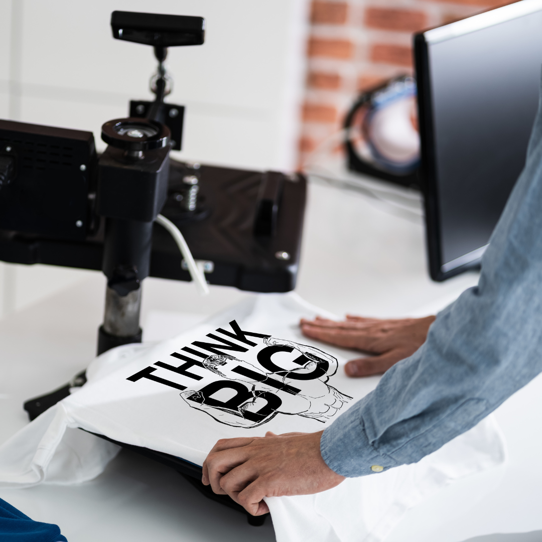 zdjęcie przedstawia białą koszulkę leżącą na maszynie, która drukuje wzór