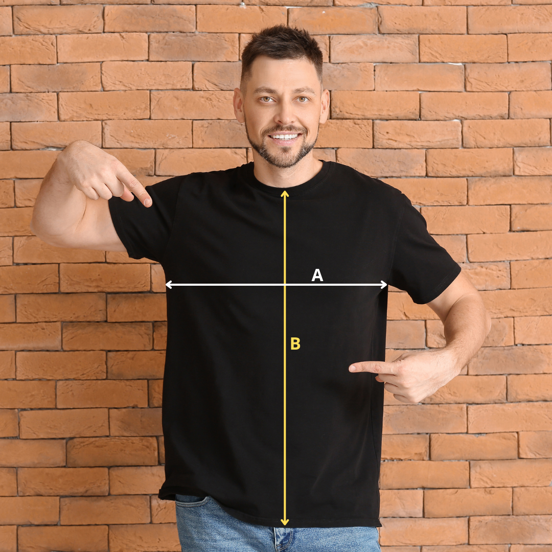 zdjęcie przedstawia uśmiechniętego mężczyznę stojącego na tle ceglanej ściany. Ubrany jest w czarną koszulkę, na której narysowane są strzałki z literami. Strzałka z literą A oznacza szerokość koszulki, strzałka z literą B oznacza długość koszulki